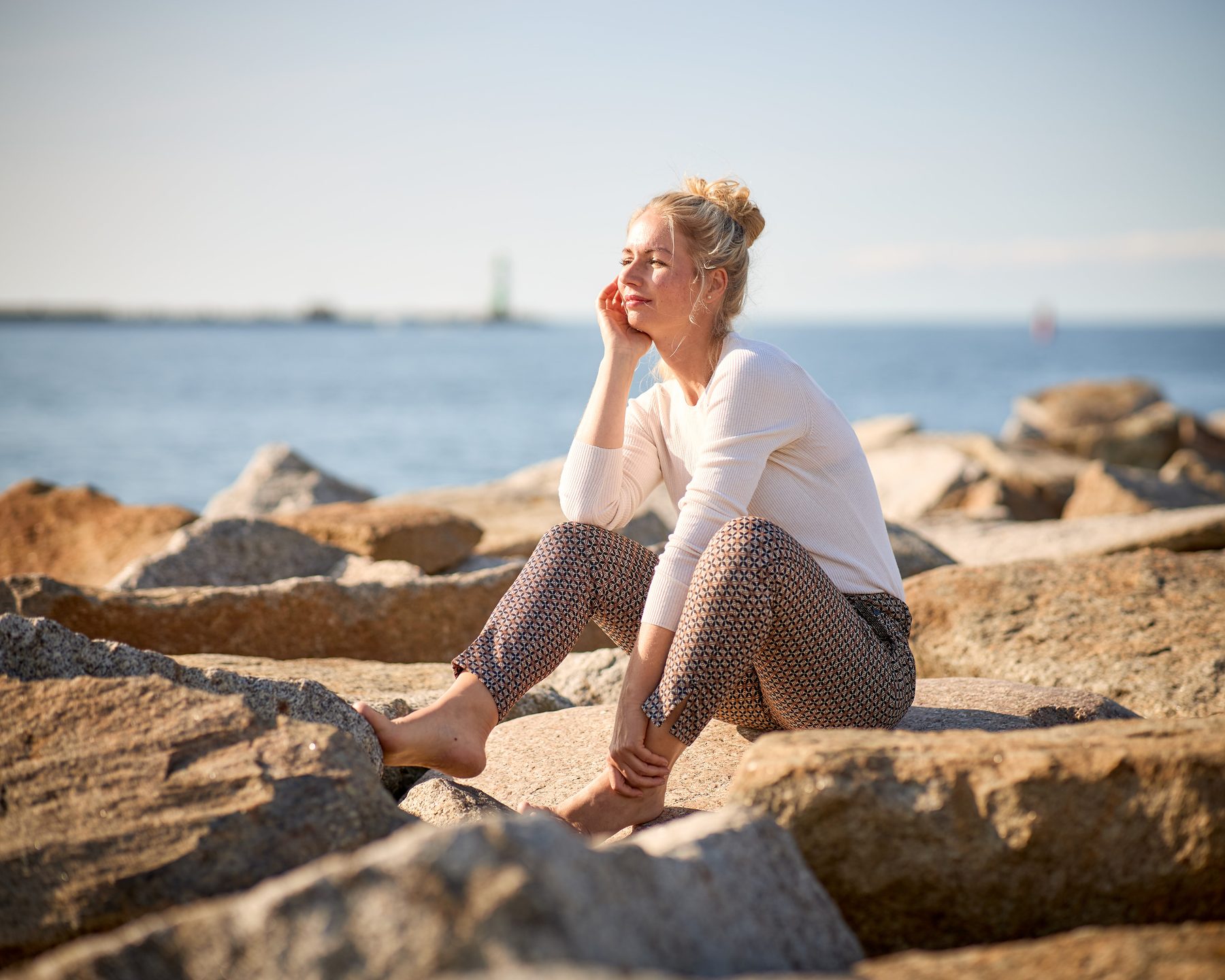 Melanie Thalmann sitzt auf Steinen am Meer und schaut in die Sonne